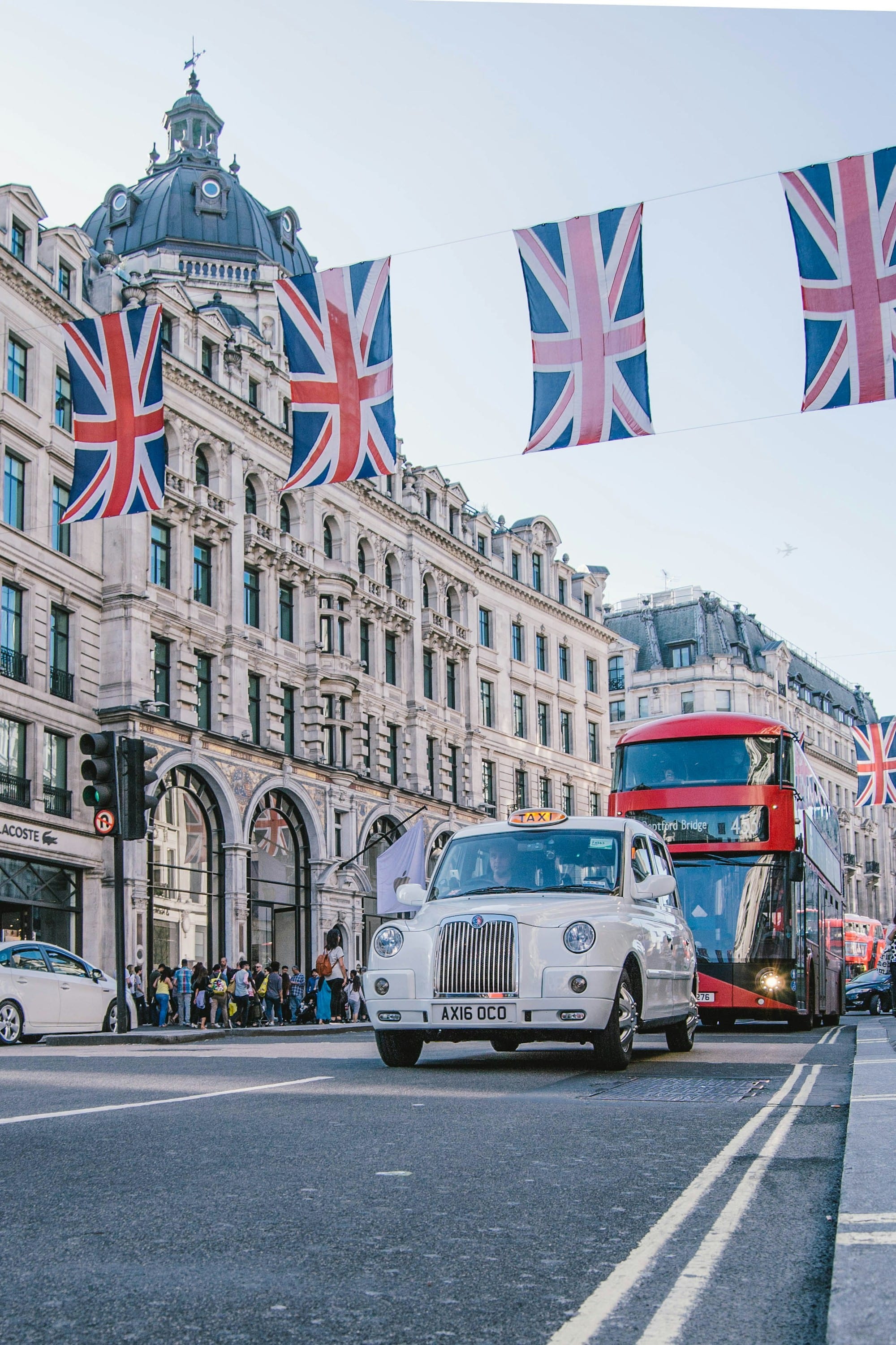 flags hung over a roadway with english cars and double decker bus