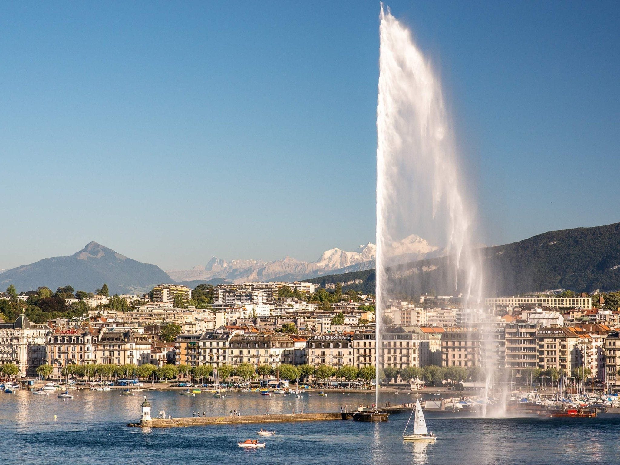 Large water fountain with buildings and boats in the background.